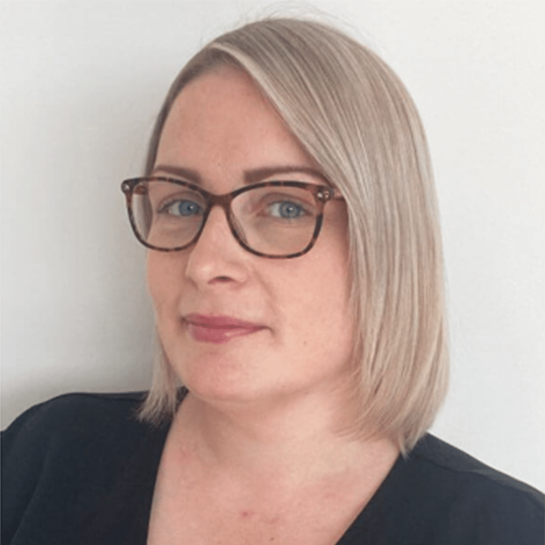 Headshot photograph of Lucy, showing her head and shoulders. She has short, straight, blonde hair and brown glasses. She is infront of a white background.